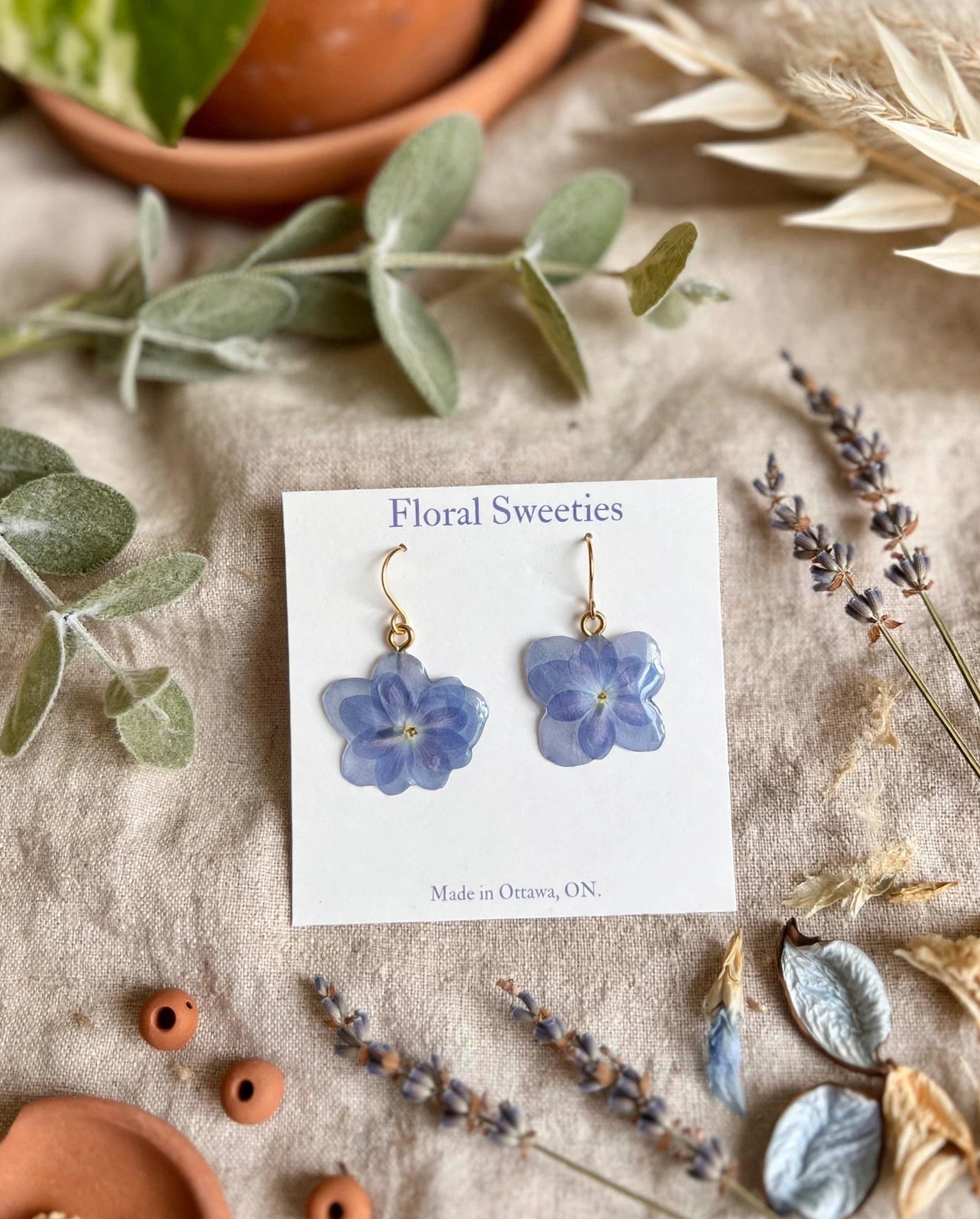 Dangle earrings with real blue hydrangea petals in resin on a display card, styled on linen