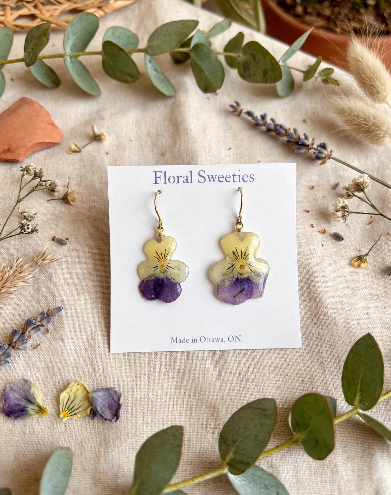 Dangle earrings with real pansy and violet flowers in resin on a display card, styled on linen