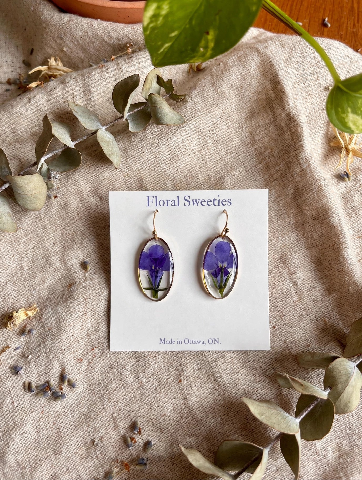 Dangle earrings with real pressed lobelia flowers in resin on a display card, styled on linen