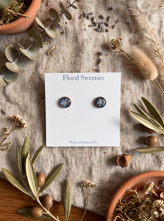 Stud earrings with real forget-me-not flowers in resin on a display card, styled on linen