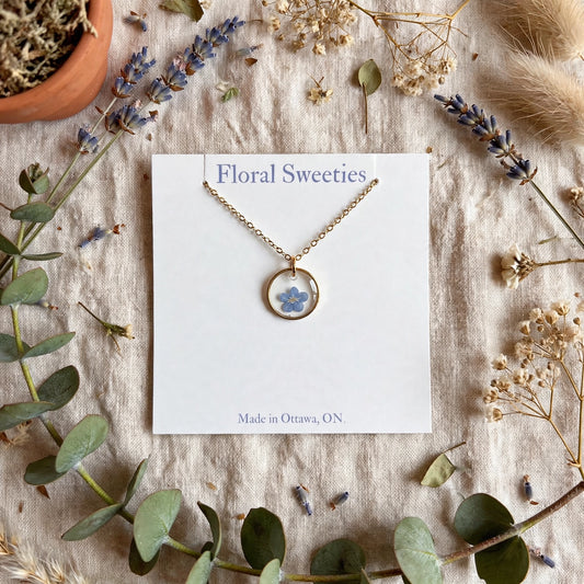 Forget-me-not flower necklace with real pressed flowers in resin on a card, styled on linen