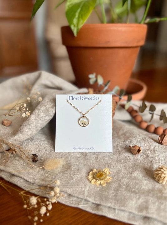 Necklace with real baby's breath flowers in a resin pendant, styled on linen