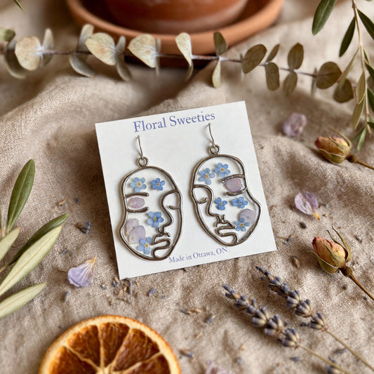 Abstract face earrings with forget-me-nots and hydrangea, angled view with dried orange slice