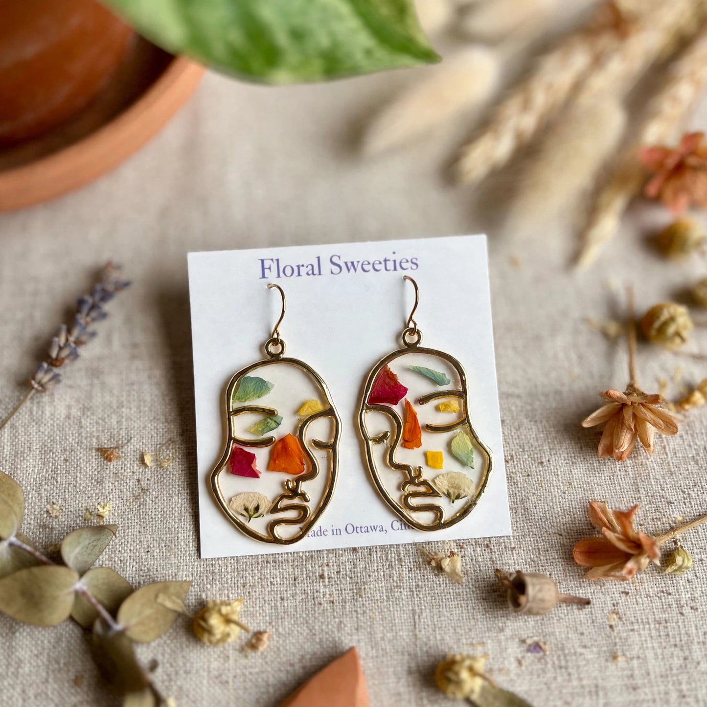 Close-up of abstract face earrings showing colorful pressed petals in resin