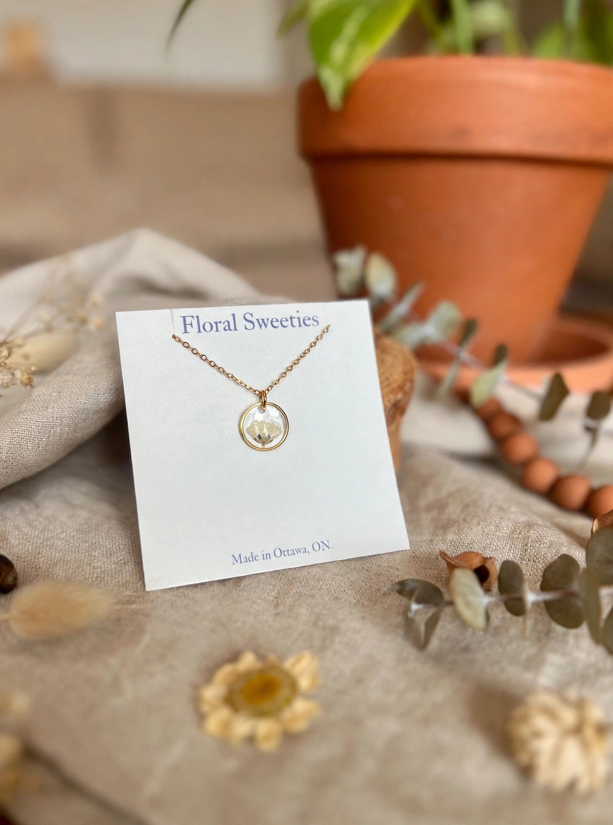 Close-up angled view of the baby's breath resin pendant necklace against draped linen