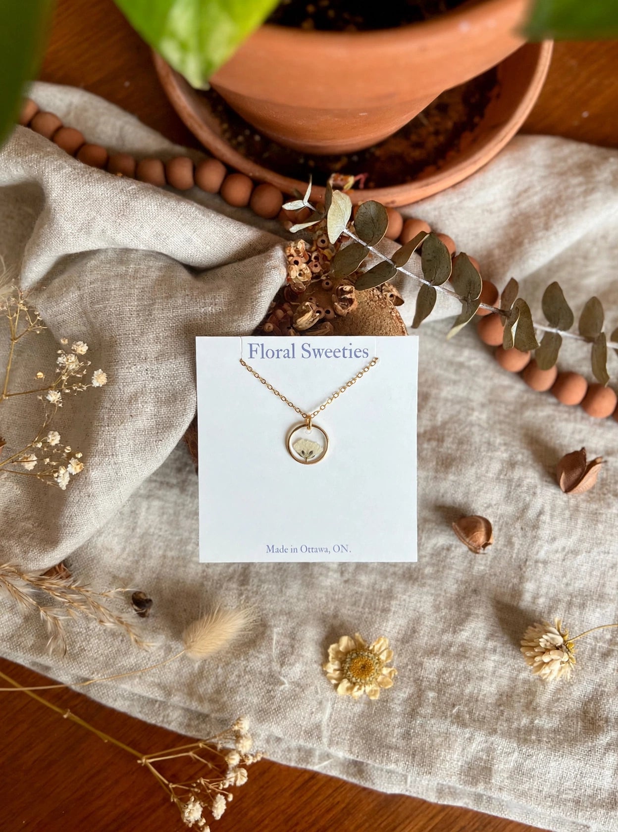 Baby's breath necklace overhead view with terracotta plant pot and wooden beads