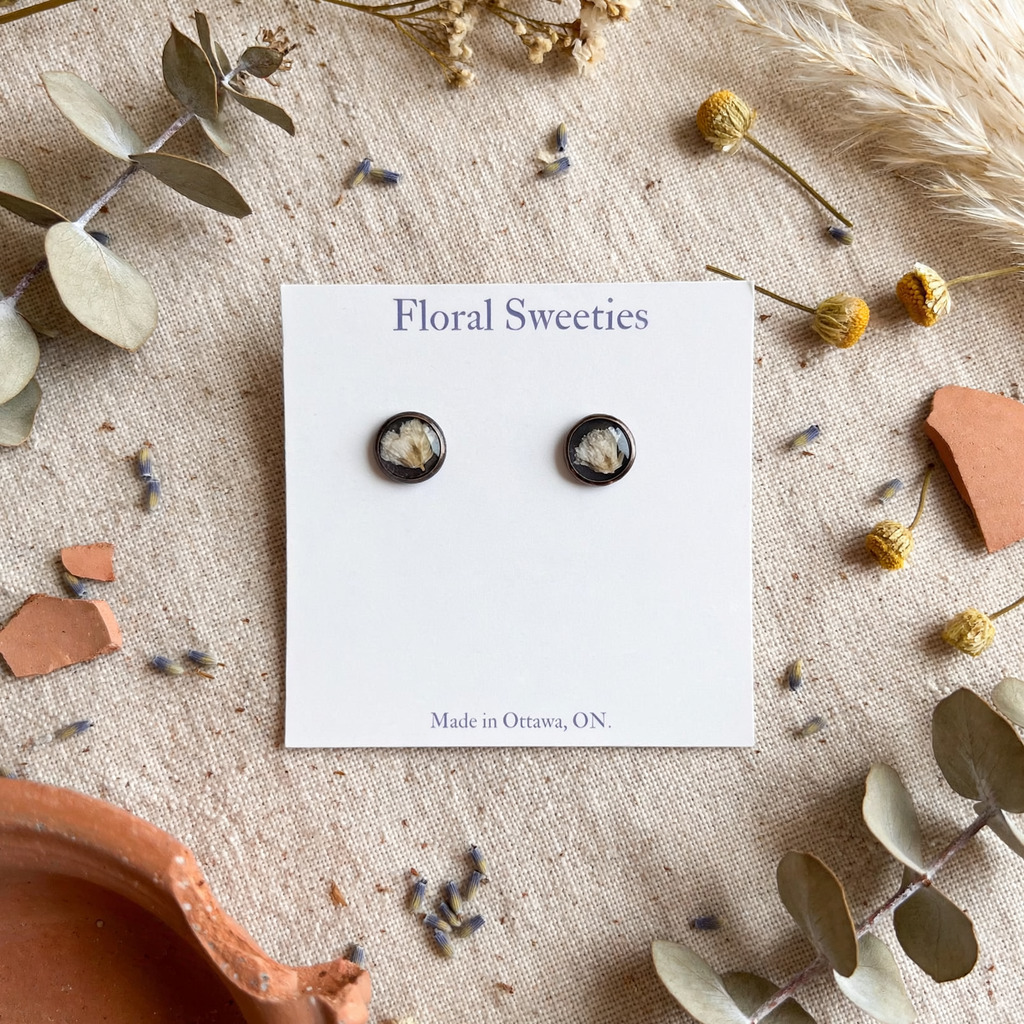 Baby's breath stud earrings on their card with eucalyptus and terracotta pieces on linen