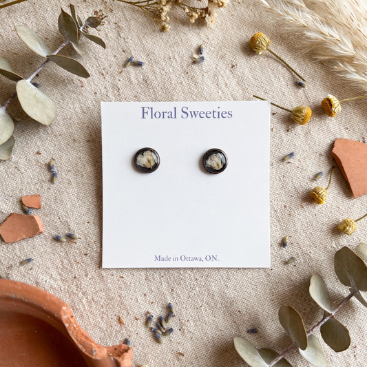 Baby's breath stud earrings on their card with eucalyptus and terracotta pieces on linen