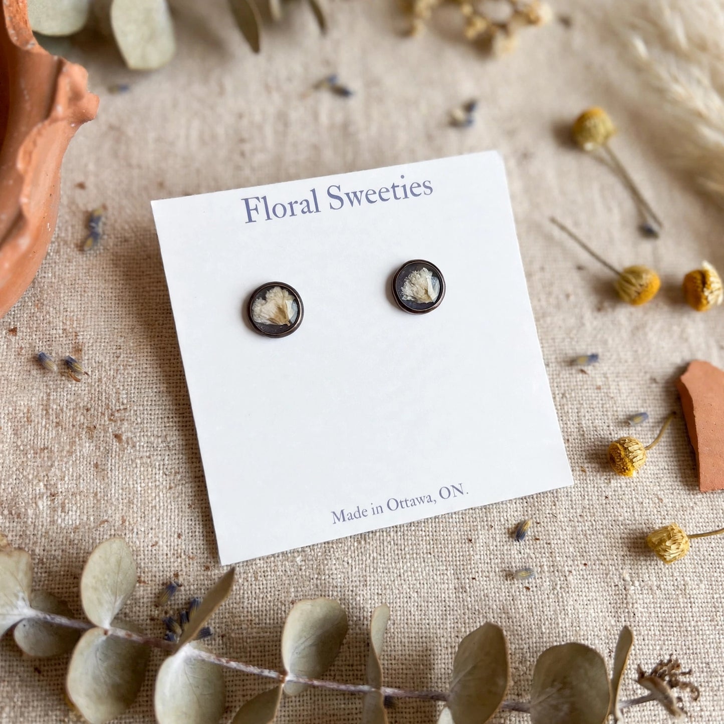 Angled close-up of baby's breath resin stud earrings on their display card