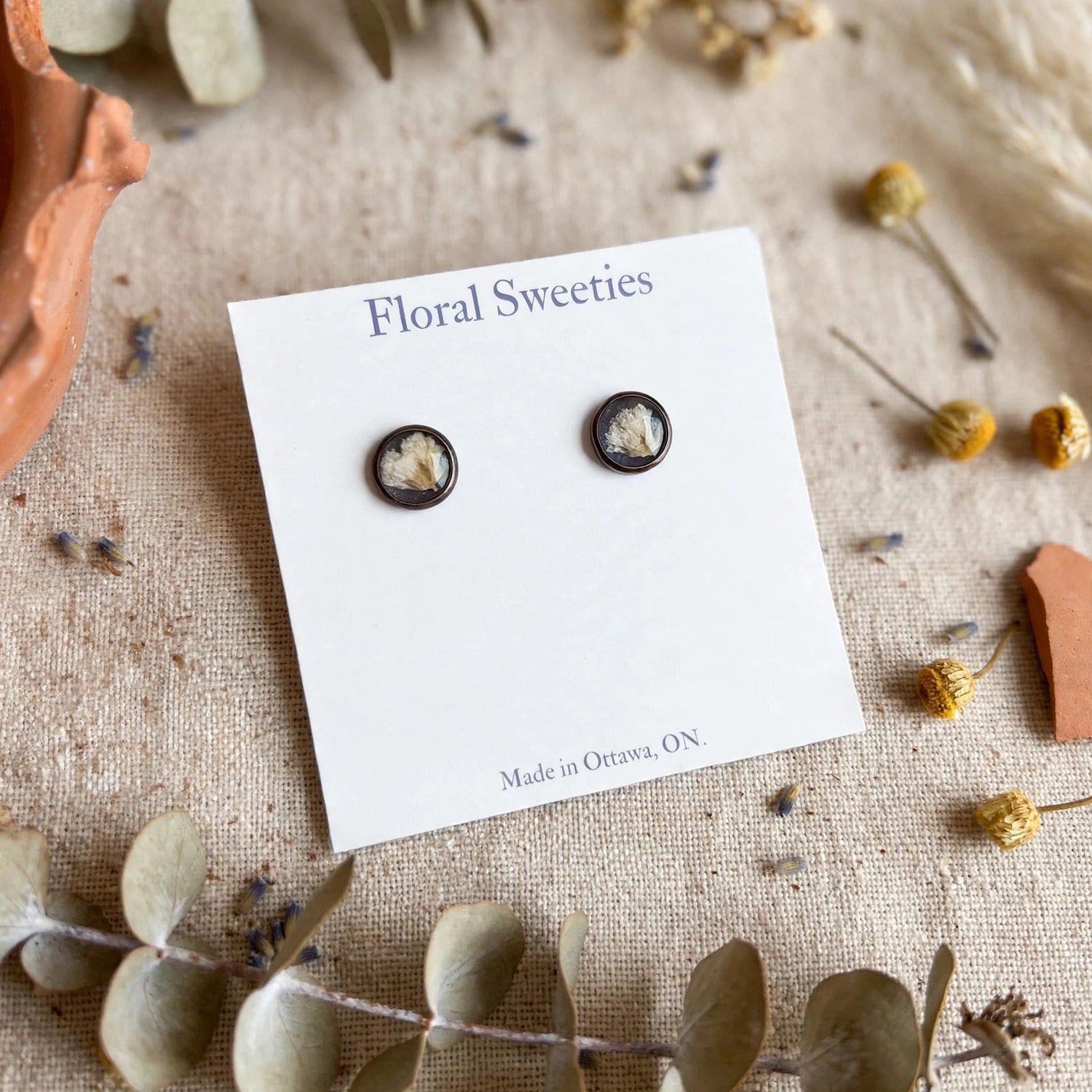 Angled close-up of baby's breath resin stud earrings on their display card
