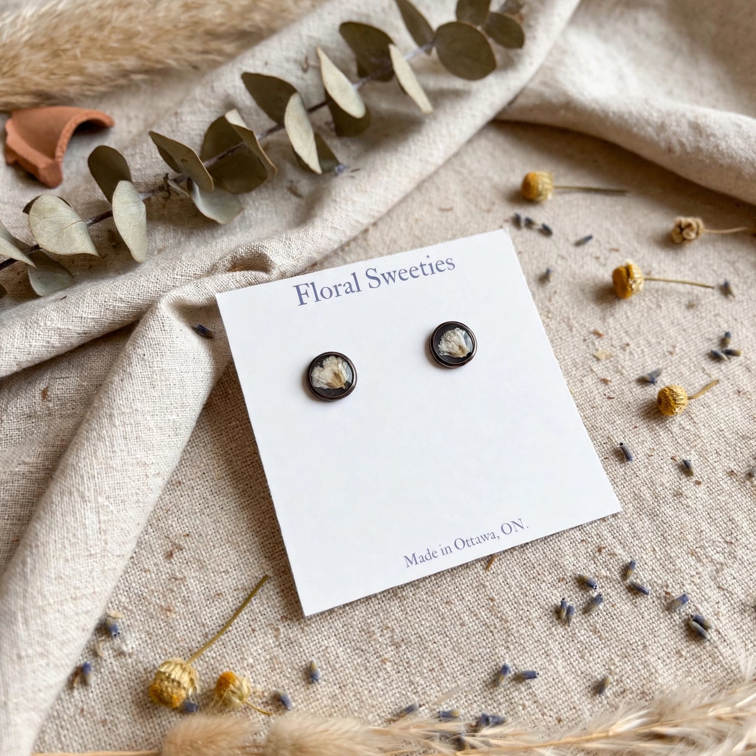 Baby's breath stud earrings on draped linen with eucalyptus, angled view