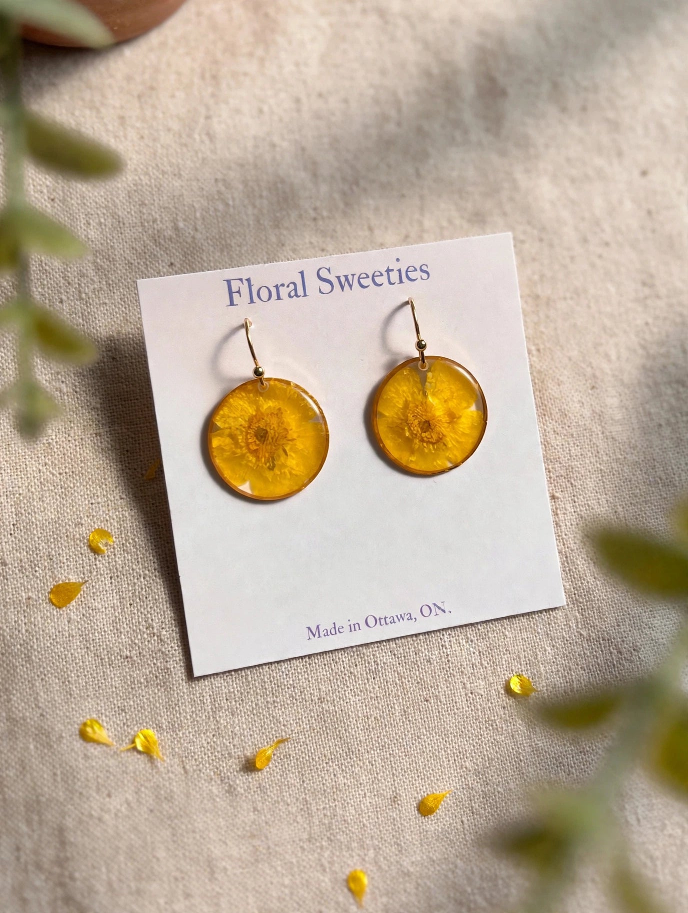Close-up angled view of buttercup flower resin dangle earrings on a display card on linen