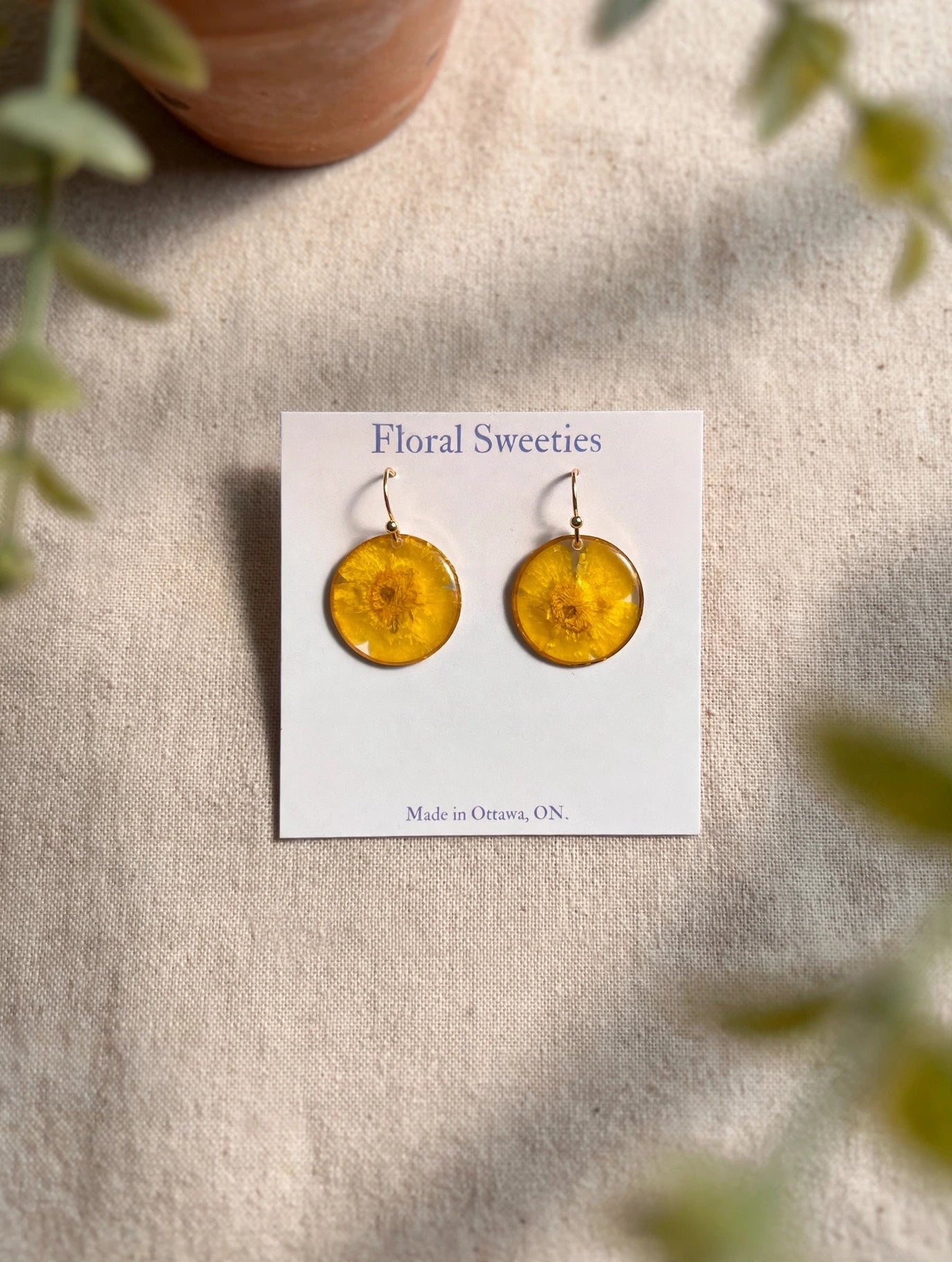 Round dangle earrings with real pressed buttercup flowers in resin on a display card, styled on linen