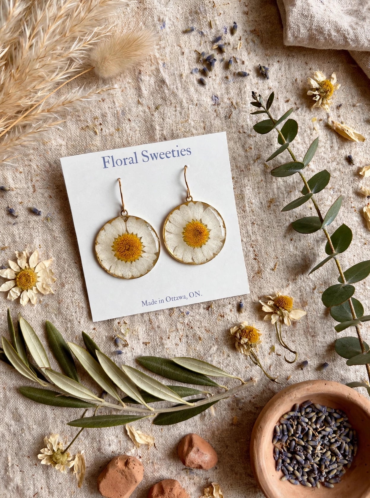 Daisy dangle earrings angled view with a bowl of lavender buds and dried daisies on linen