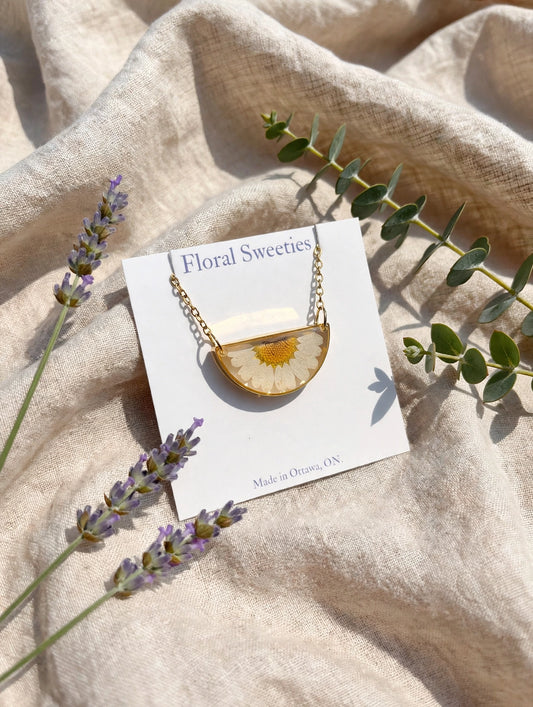 Angled view of the daisy resin pendant necklace on its display card with lavender and eucalyptus on linen