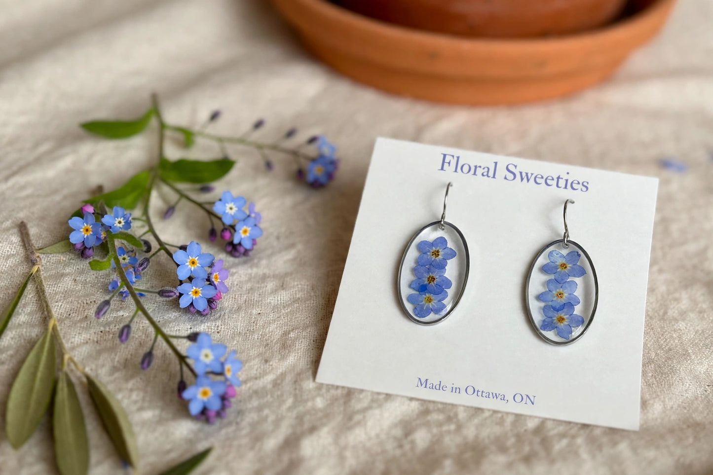 Close-up of forget-me-not dangle earrings showing three tiny flowers in each oval resin drop