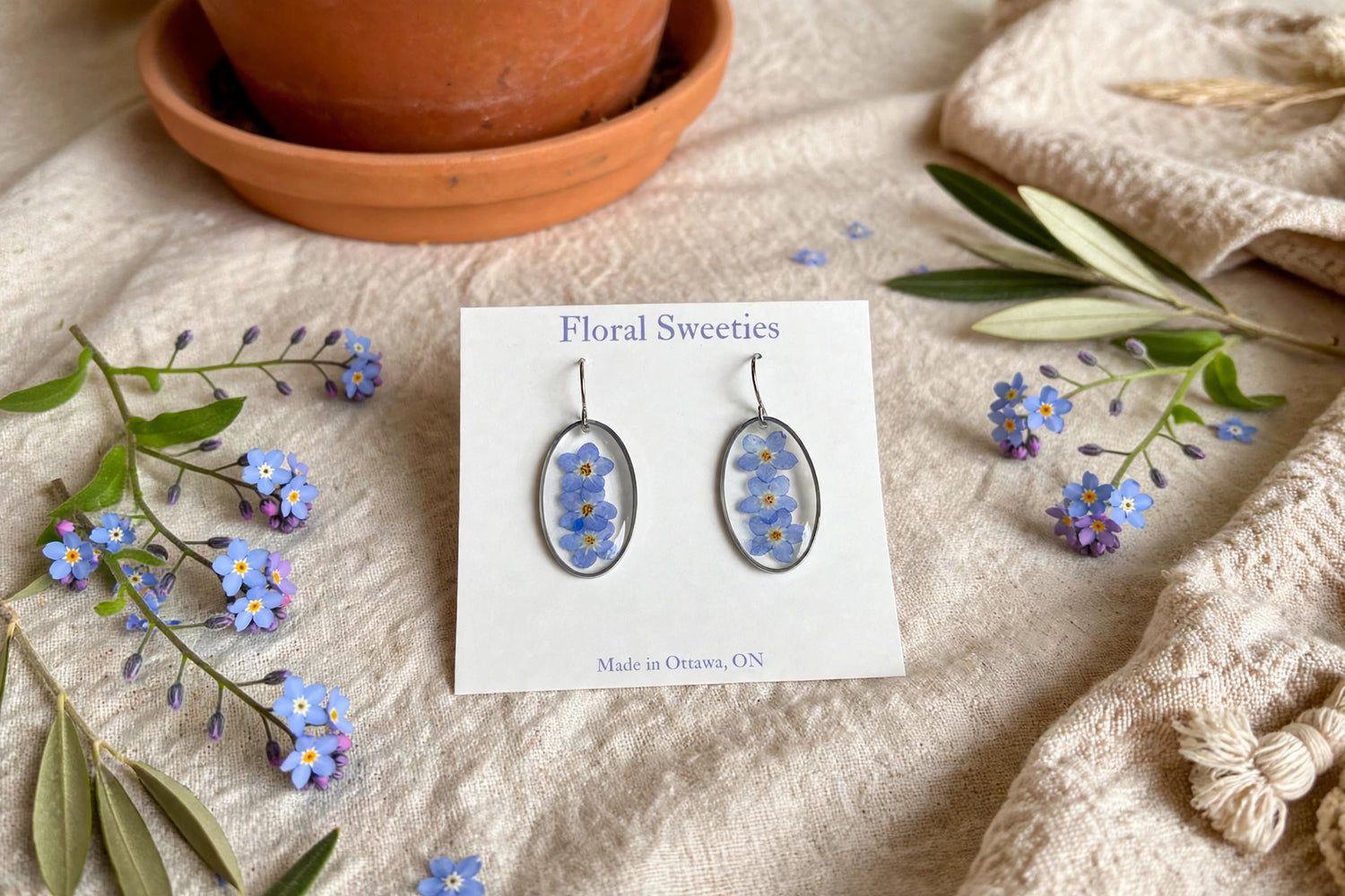 Dangle earrings with real forget-me-not flowers in resin on a display card, styled on linen