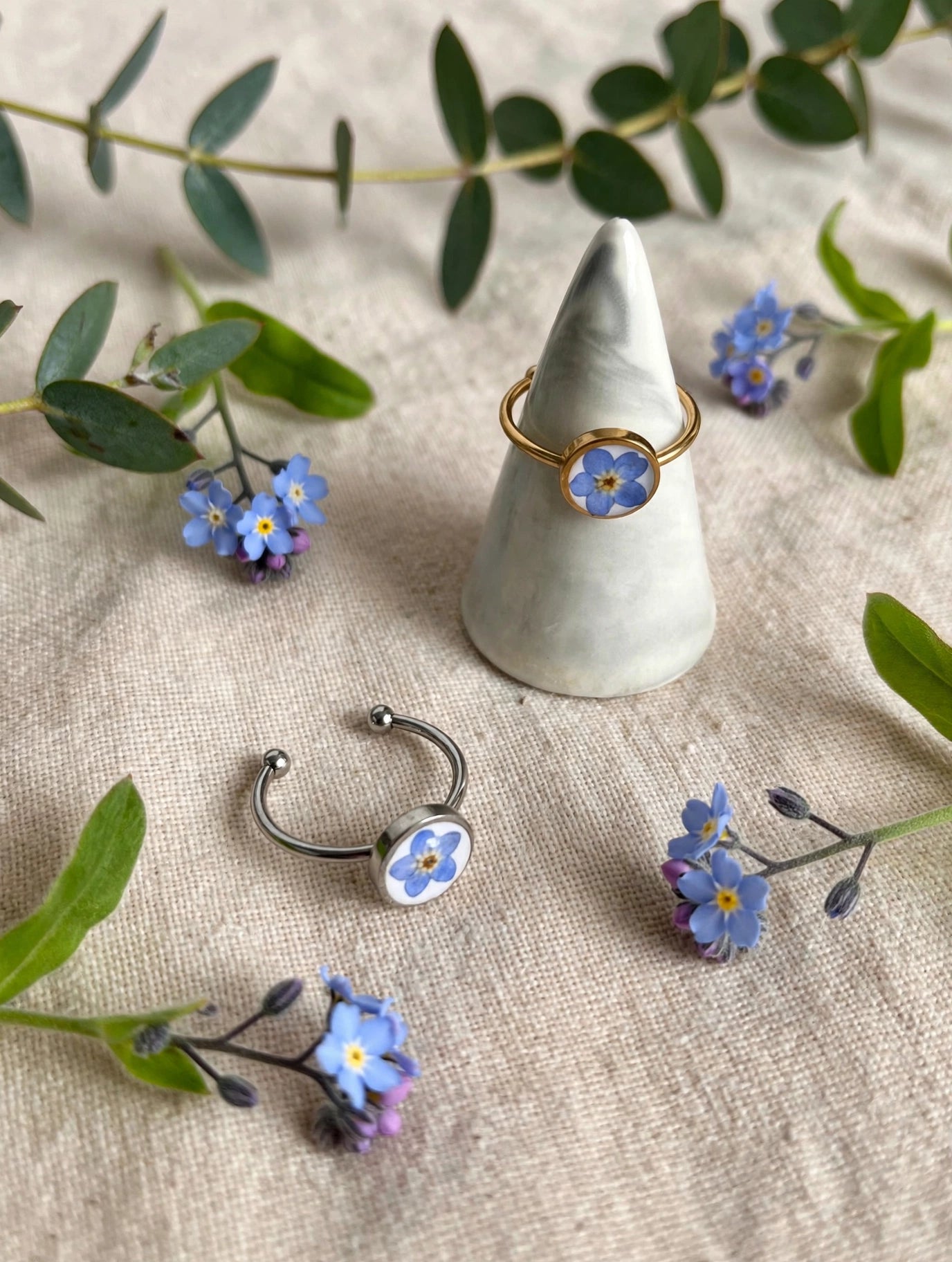 Adjustable rings with real forget-me-not flowers in resin, silver and gold, styled on linen