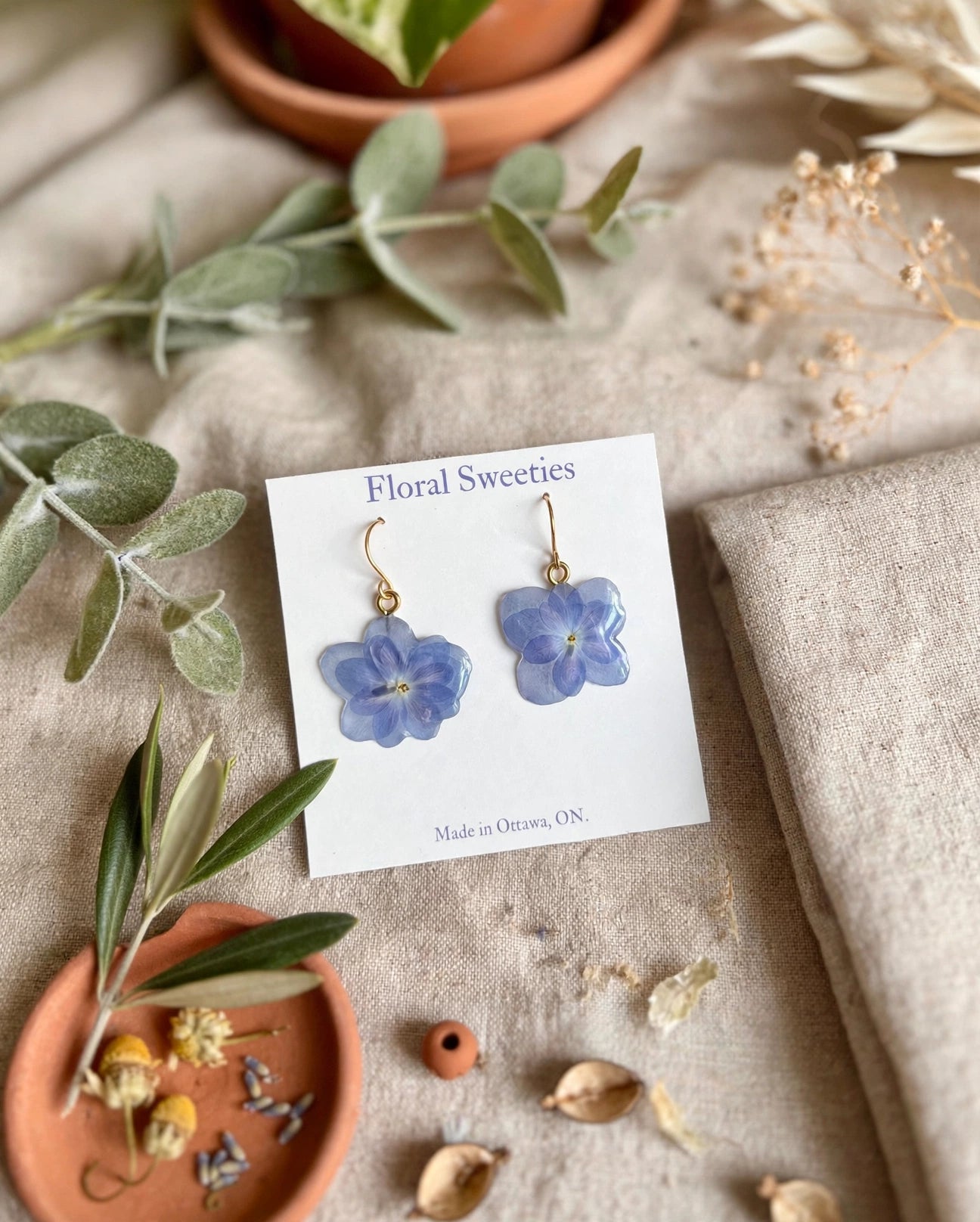 Hydrangea dangle earrings angled view with a small terracotta dish on linen