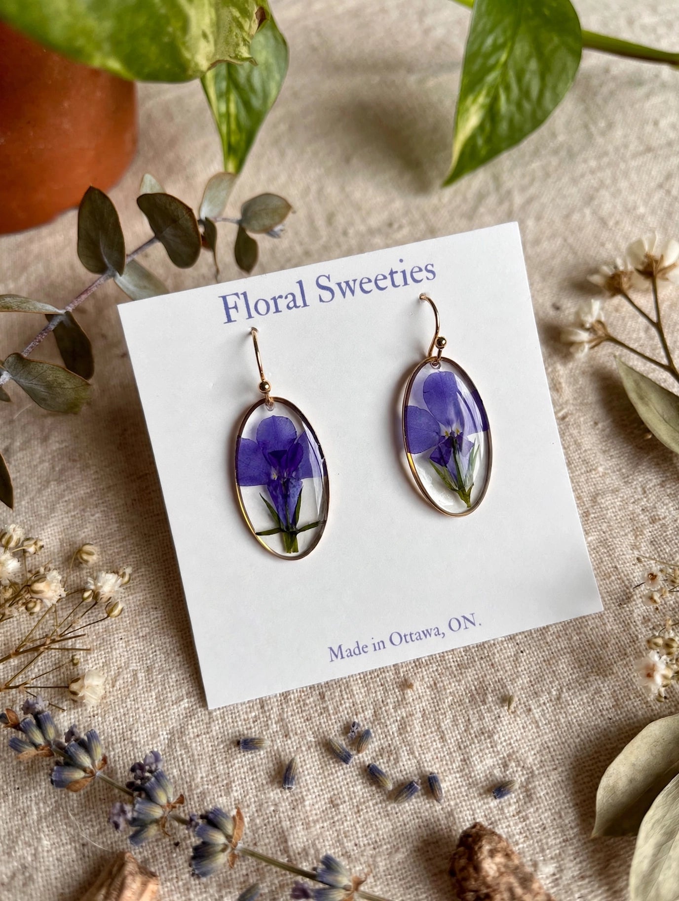 Close-up angled view of oval lobelia resin dangle earrings on their display card
