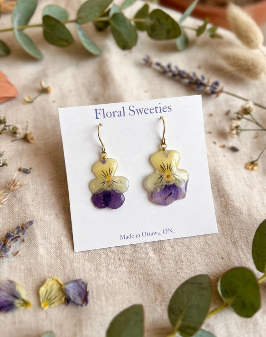 Pansy and violet dangle earrings angled view with loose pansy flowers on linen