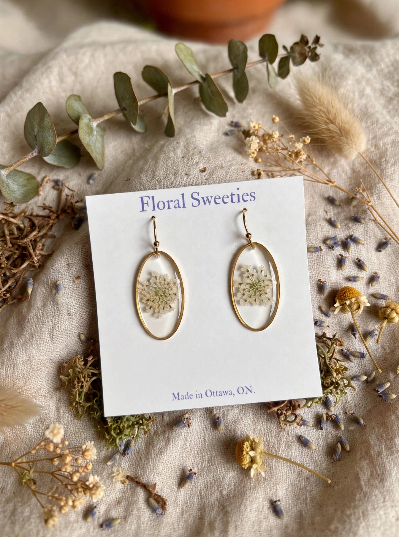 Close-up front view of Queen Anne's lace resin dangle earrings on their card