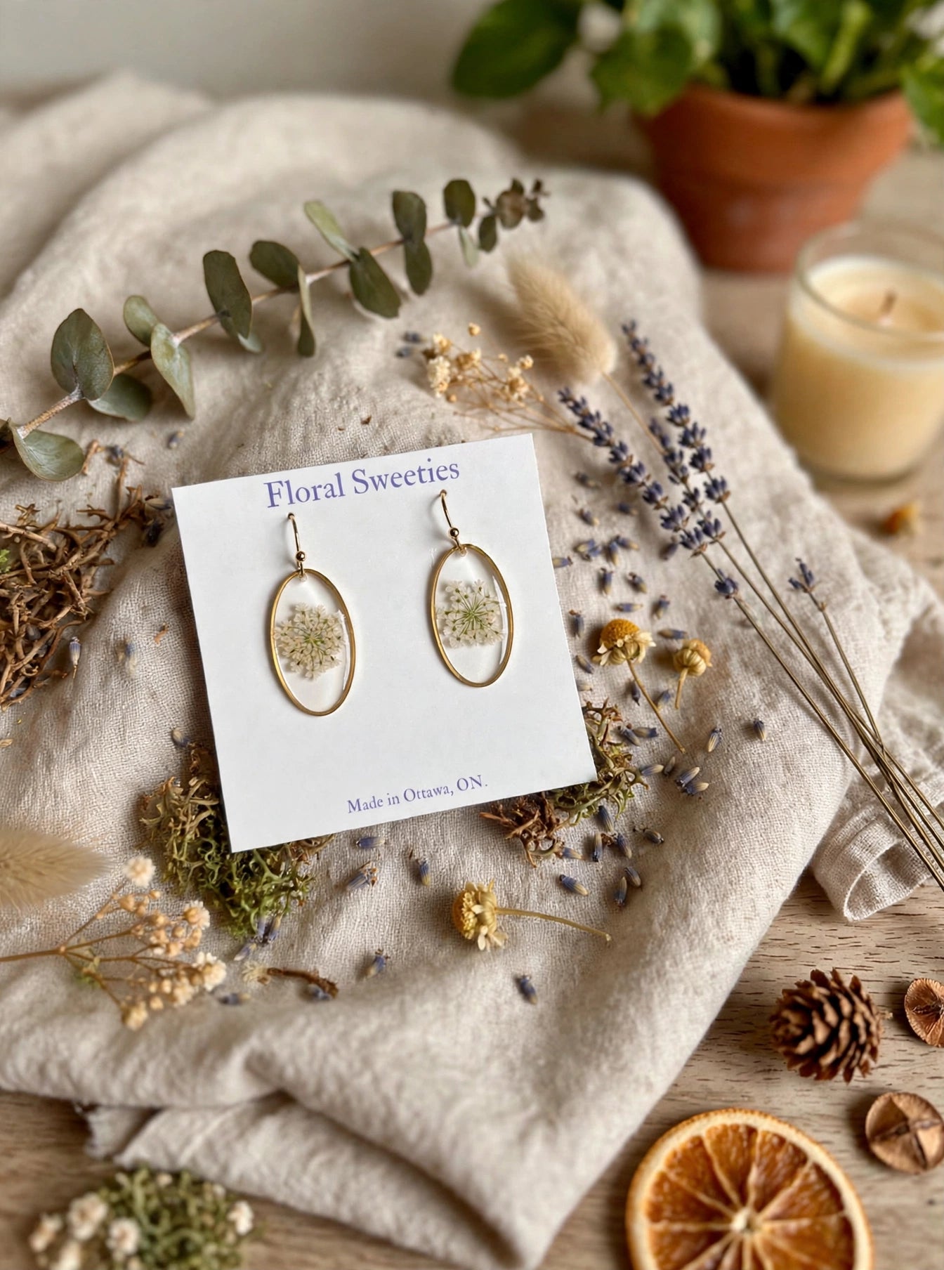 Queen Anne's lace earrings styled on draped linen with a candle and pinecone